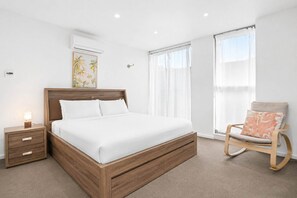 Ein Schlafzimmer mit einem hölzernen Bett, einem Nachttisch, einem Sessel und einem Fenster mit Vorhängen.