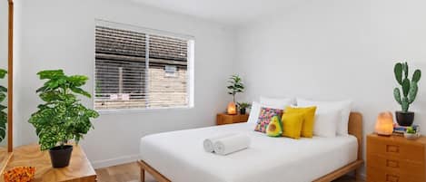 A bedroom with a bed, a window, a nightstand, a dresser, and a potted plant.