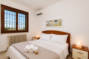 Ein Hotelzimmer mit einem Bett, einem Heizkörper, einem Fenster mit Gitterstäben, einem Bild und einem Nachttisch mit Lampe.
