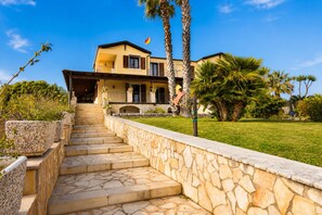 A two-story house with a stone staircase leading to the entrance, surrounded by a well-maintained lawn and palm trees. - Villa in Donnalucata with 4 bedrooms sleeps 10 (Donnalucata)