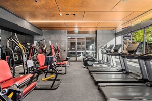 Ein Fitnessstudio mit verschiedenen Trainingsgeräten, darunter Laufbänder und Kraftgeräte, sowie einem Glastür-Eingang.