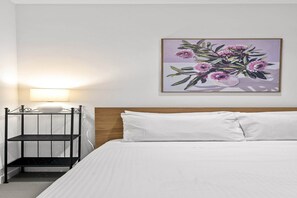 Ein Hotelzimmer mit einem Bett, einem Nachttisch mit Lampe und einem Wandbild mit Blumenmotiven.