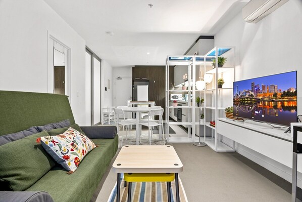 A modern living room with a green sofa, a small wooden table, and a TV displaying a cityscape. - City-View 2-Bed Apartment Melbourne CBD (Melbourne)