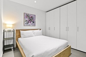 A bedroom with a bed, a nightstand, a lamp, a wardrobe, and a wall-mounted picture. - City-View 2-Bed Apartment Melbourne CBD (Melbourne)