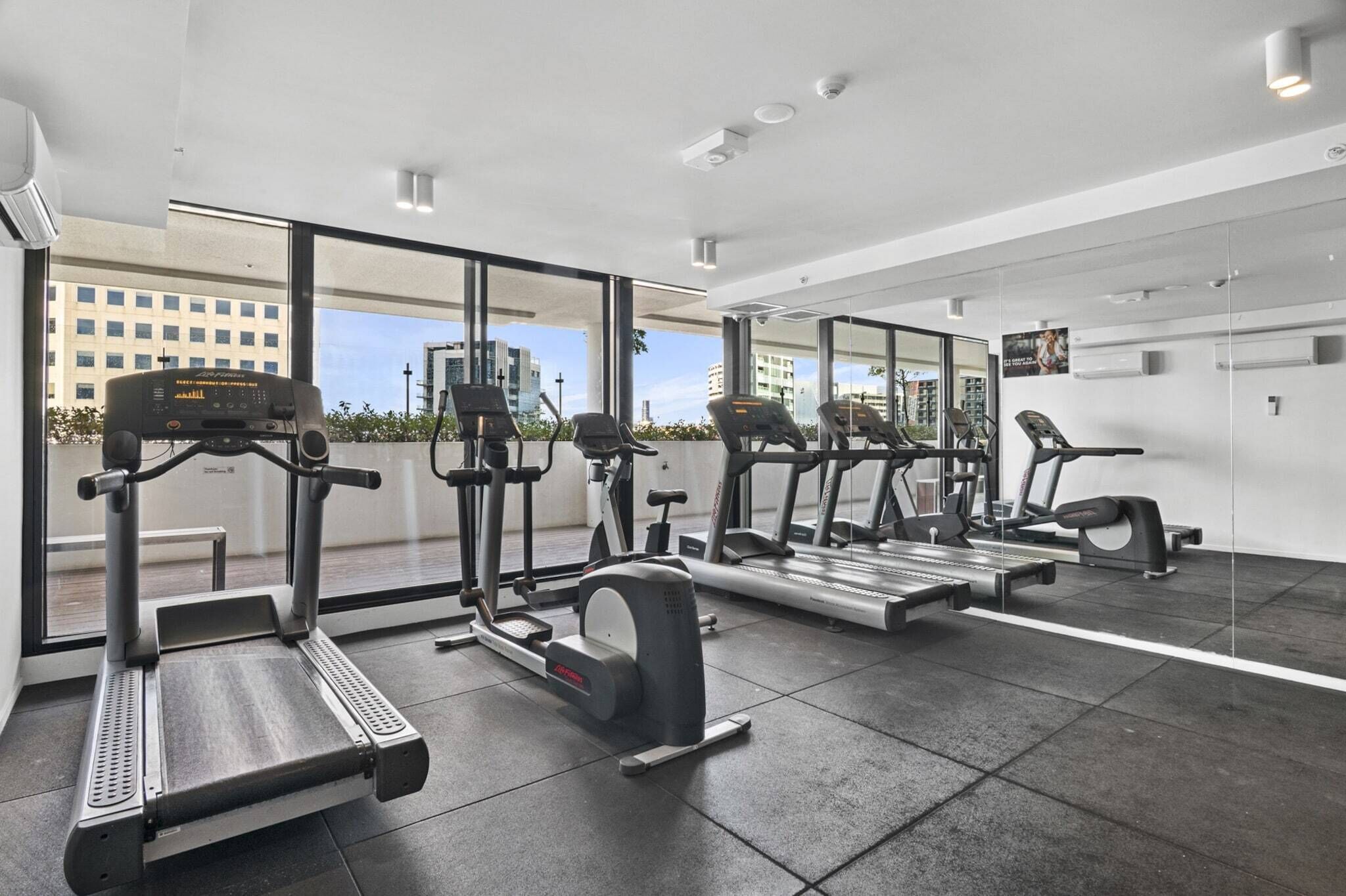 Un gimnasio moderno con equipos de cardio variados, ventanas amplias y vistas a la ciudad.