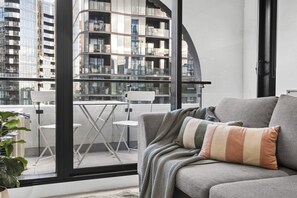 Ein Balkon mit einer grauen Couch, einem gestreiften Kissen und einem Blumentopf.