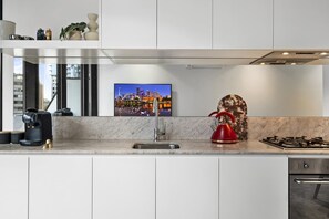 Eine moderne Küche mit einer Spüle aus Edelstahl, einem roten Wasserkocher und einem Stadtbild an der Wand.