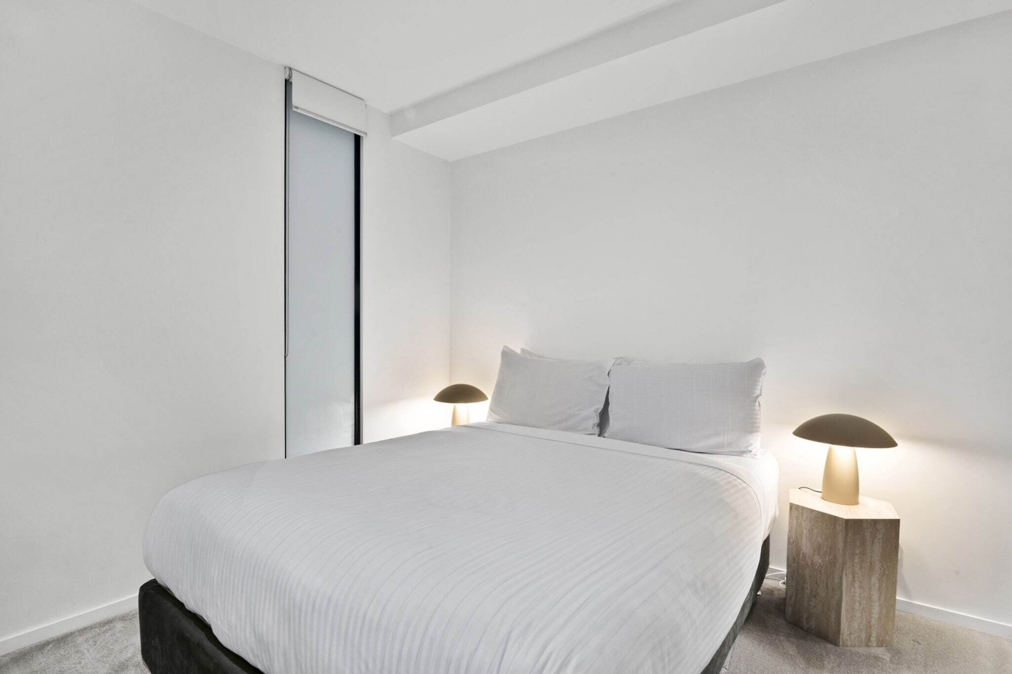 Quarto minimalista com cama, duas luminárias de cabeceira e uma porta de correr.