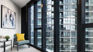 Een modern interieur met een groot raam, een grijze bank met een gele kussen en een tafel met een zwart frame.