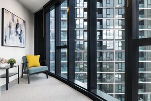 A modern interior with a large window, a grey sofa with a yellow cushion, and a black-framed table. - High-Rise 1-Bed Apartment Near Docklands (Melbourne)