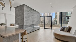 Een modern interieur met een keukenhoek, een zithoek met een bank en kussens, en een uitzicht op de stad door grote ramen.