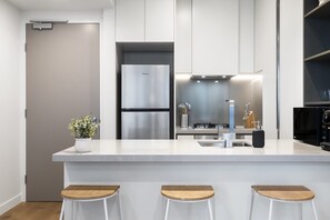 Une cuisine moderne dotée d’un îlot central, d’appareils électroménagers en acier inoxydable et de tabourets de bar.