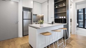 Een moderne keuken met een centraal eiland, barstoelen, een inbouwoven en een koffieapparaat.