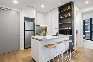 A modern kitchen with a central island, bar stools, a built-in oven, and a coffee machine. - High-Rise 1-Bed Apartment Near Docklands (Melbourne)