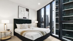 Een moderne slaapkamer met een groot bed, twee nachtkastjes, uitzicht op de stad en een groot raam.