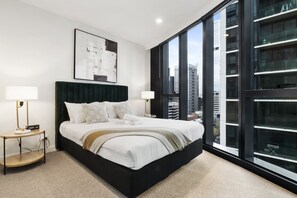 A modern bedroom with a large bed, two bedside tables, a city view, and a large window. - High-Rise 1-Bed Apartment Near Docklands (Melbourne)