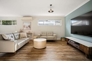 A living room with a sofa, armchair, ottoman, and a large flat-screen TV. - Luxury Waterfront 5-Bed Family Home Near Mandurah (Halls Head)