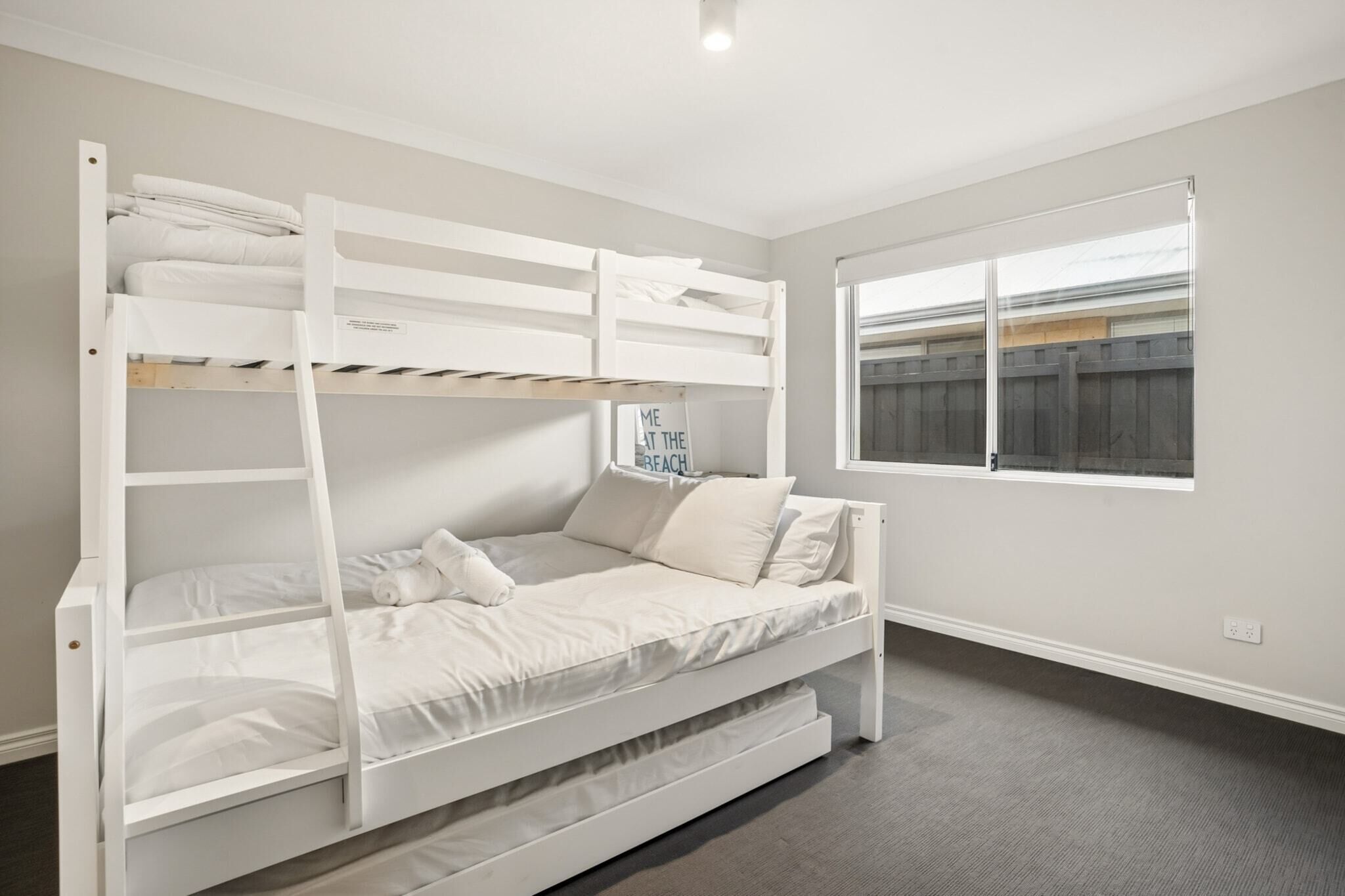 Un lit superposé avec un lit inférieur, une fenêtre donnant sur une clôture et une prise électrique au mur.