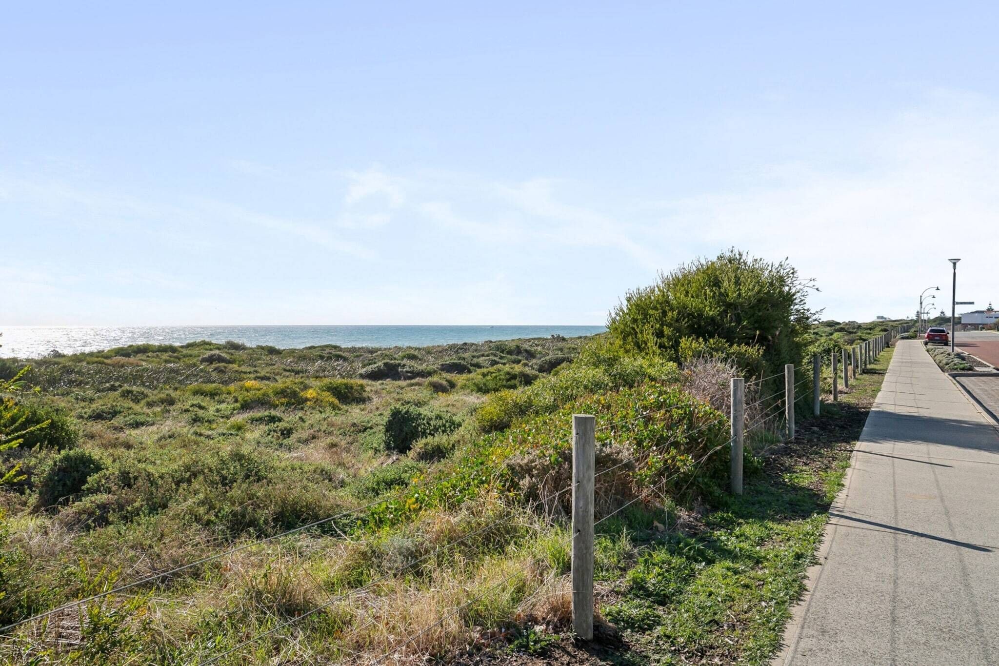 Une promenade en bord de mer offrant une vue sur l’océan, bordée de végétation et entourée d’une clôture.