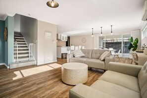 A modern living room with a sofa, ottoman, and a staircase leading to an upper level. - Luxury Waterfront 5-Bed Family Home Near Mandurah (Halls Head)