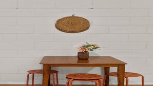 Een houten eettafel met vier krukken, een vaas met bloemen en een geweven wanddecoratie.