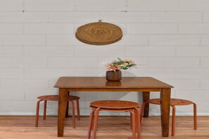 Ein Holztisch mit vier Hockern, eine Vase mit Blumen und ein gewebter Wandbehang.