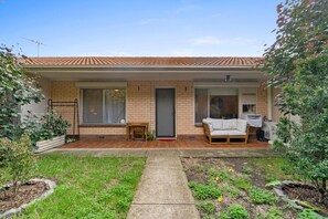 Ein Wohnhaus mit Ziegeldach, einer Veranda, einem kleinen Garten und einem weißen Außenbereich mit Sitzgelegenheiten.