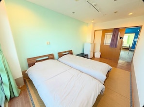 Una camera d'albergo con due letti, un comodino, una lampada e vista sul corridoio.