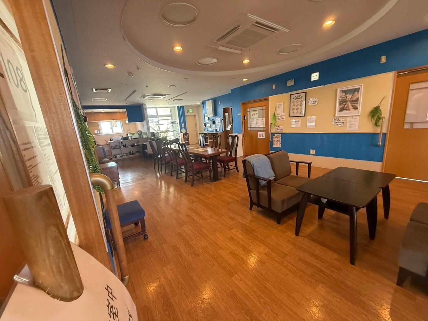 A dining area with wooden flooring, tables, chairs, and a blue accent wall.