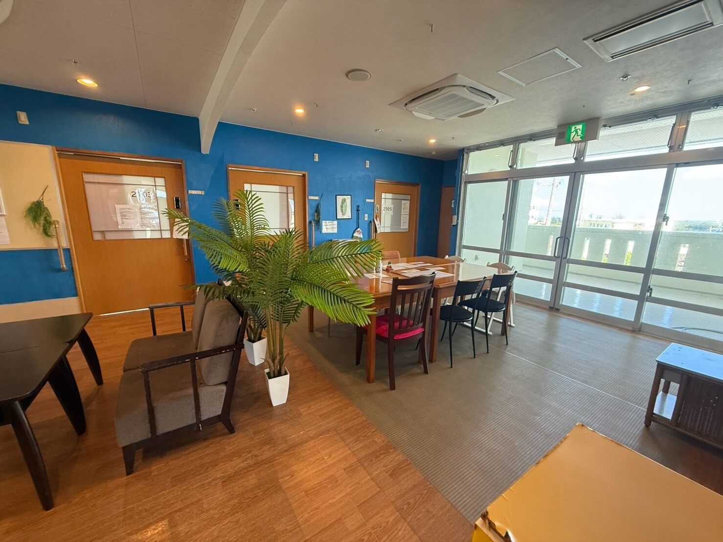 A hotel room with a large window, a wooden floor, a dining area with chairs and a table, and a potted plant.