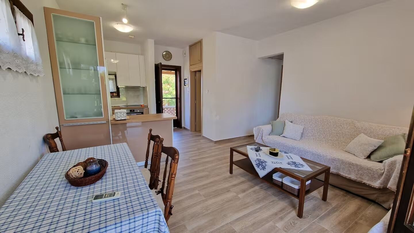 Een woonkamer met een bank, een salontafel en een eettafel met stoelen. Achtergrond is een keuken.