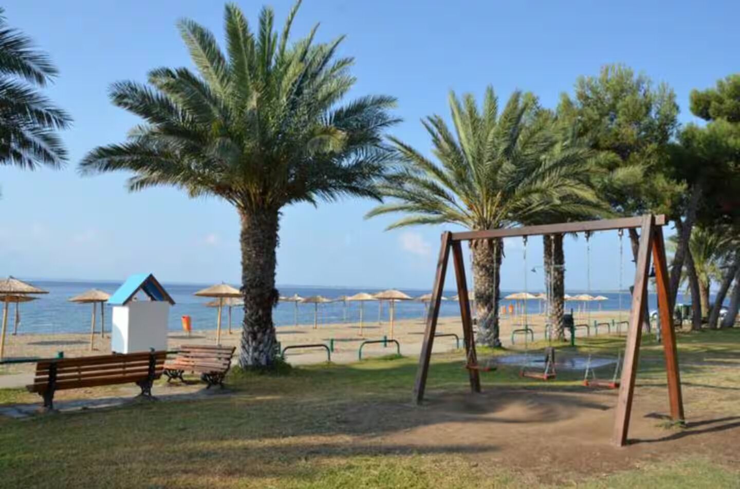 Ein Park direkt am Strand mit Schaukeln, Bänken und Sonnenschirmen.