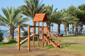 A wooden play structure with a slide and stairs, surrounded by palm trees and a view of the sea. - Halikidiki, Family house to enjoy by the beach (Kalives Polygyrou)