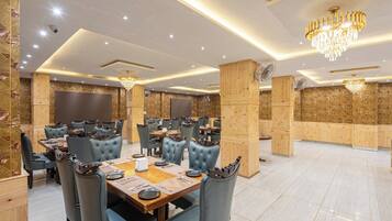 A spacious dining area with multiple tables and chairs, wooden accents, and modern lighting fixtures.