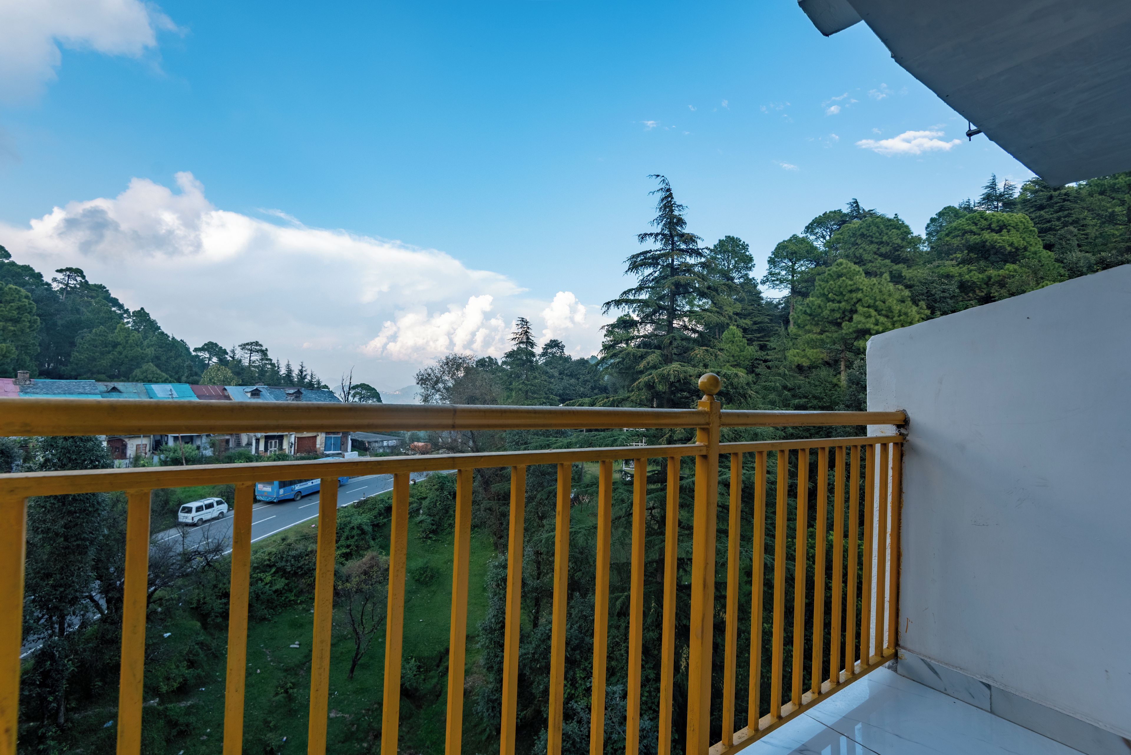 A balcony with a yellow railing overlooking a road and dense greenery.