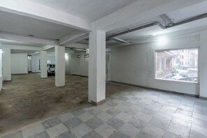 A spacious indoor area with a high ceiling, visible structural columns, and a large window offering a view of the outside.
