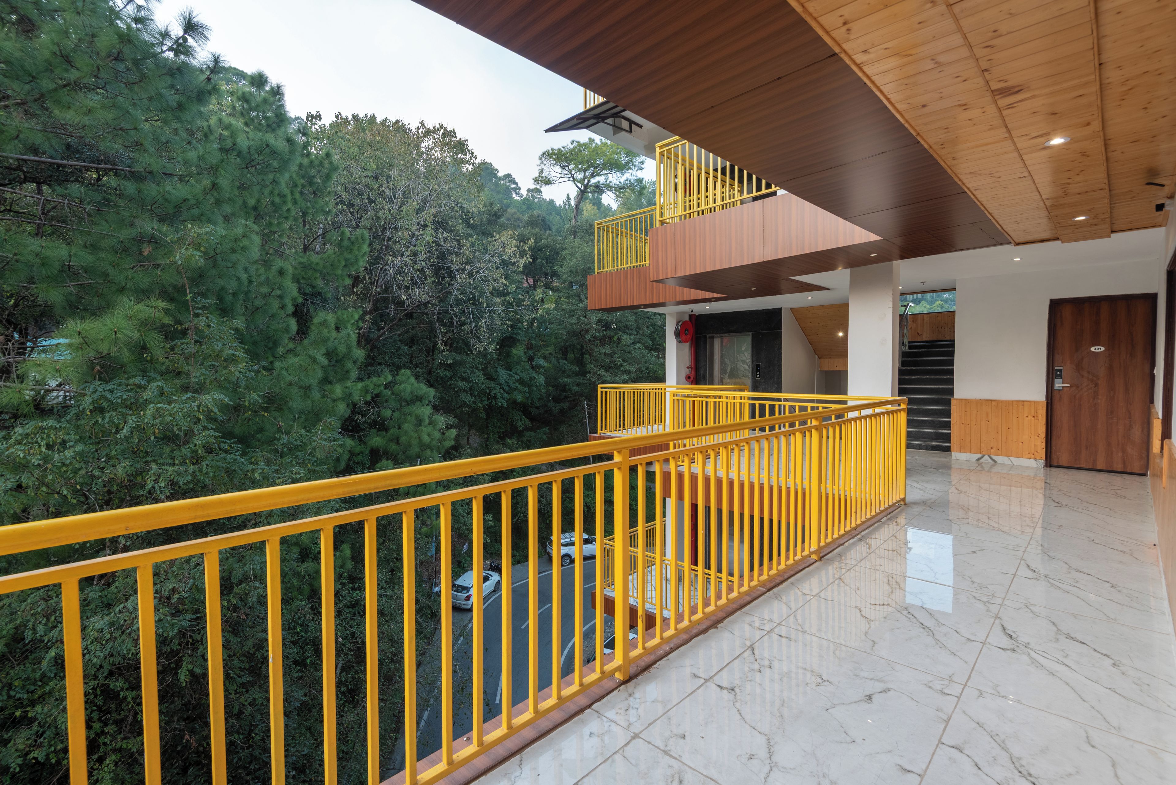 A modern building with a yellow railing, a wooden interior, and a view of trees.