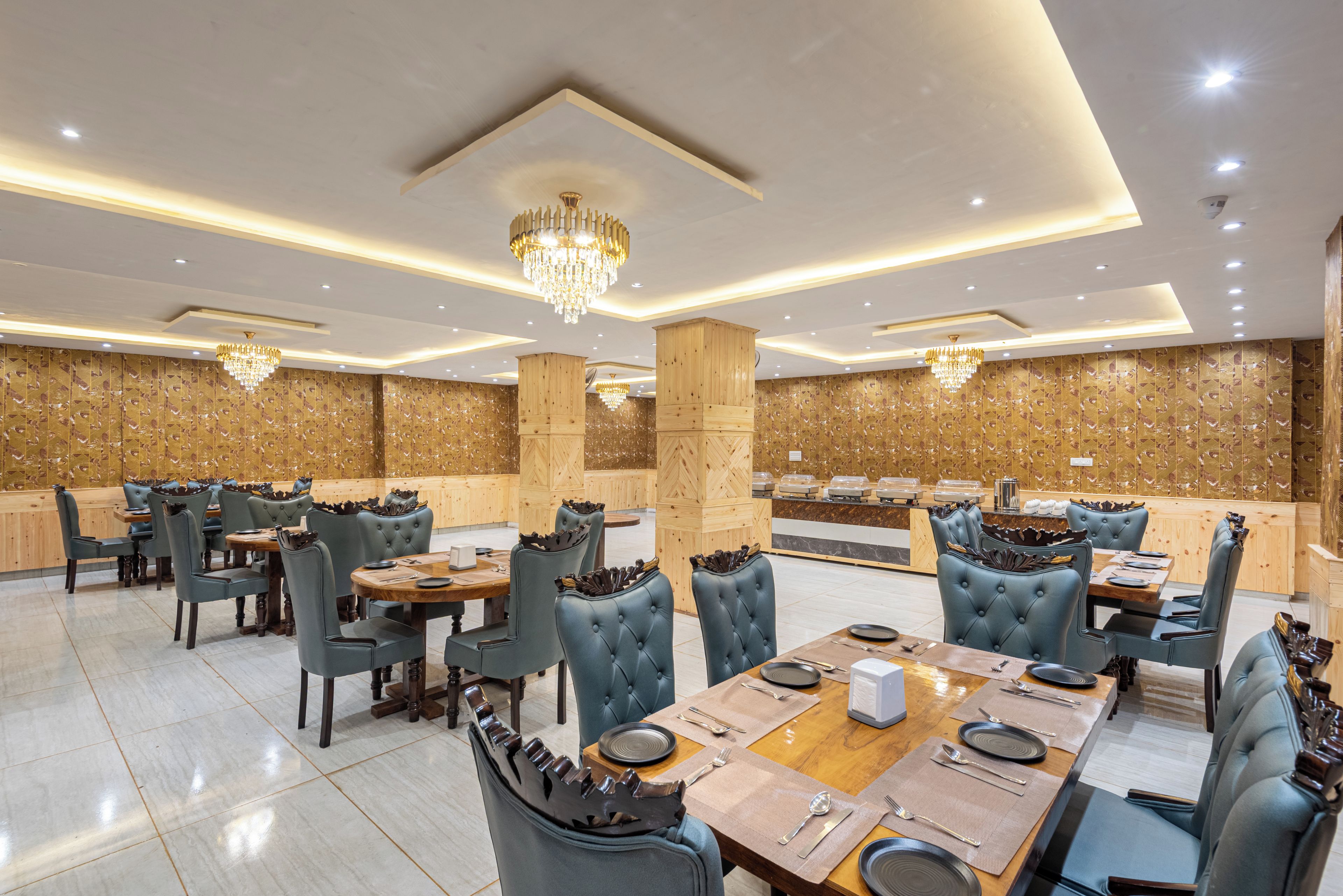 Un comedor amplio con techos altos, candelabros y paneles de madera. Las mesas están dispuestas con platos, cubiertos y servilletas.