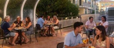 Un espacio de comedor al aire libre con mesas y sillas, rodeado por un corredor cubierto.