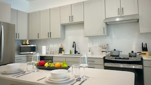 A modern kitchen with white cabinets, a stainless steel refrigerator, a microwave, a stove, and a fruit bowl on the counter. - Near Texoma Med 1BR Quiet with Pool Gym (Sherman)