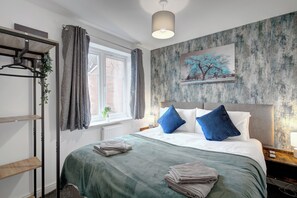 Een slaapkamer met een bed, kussens, een raam, een radiator, een plant en een muur met een structuur.