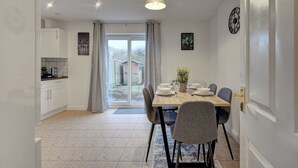 Una cocina moderna con armarios blancos, un comedor con mesa dispuesta para cuatro personas y vistas al exterior a través de un ventanal.