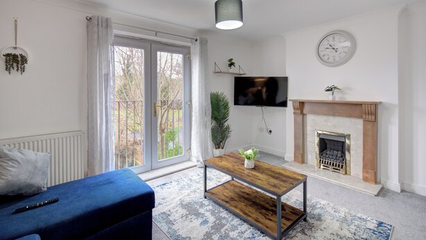 Una sala de estar con un sofá, una mesa de centro, una chimenea, un televisor y un ventanal grande.