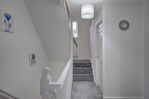 A staircase with a white railing and carpeted steps leading to a door with a decorative mirror.