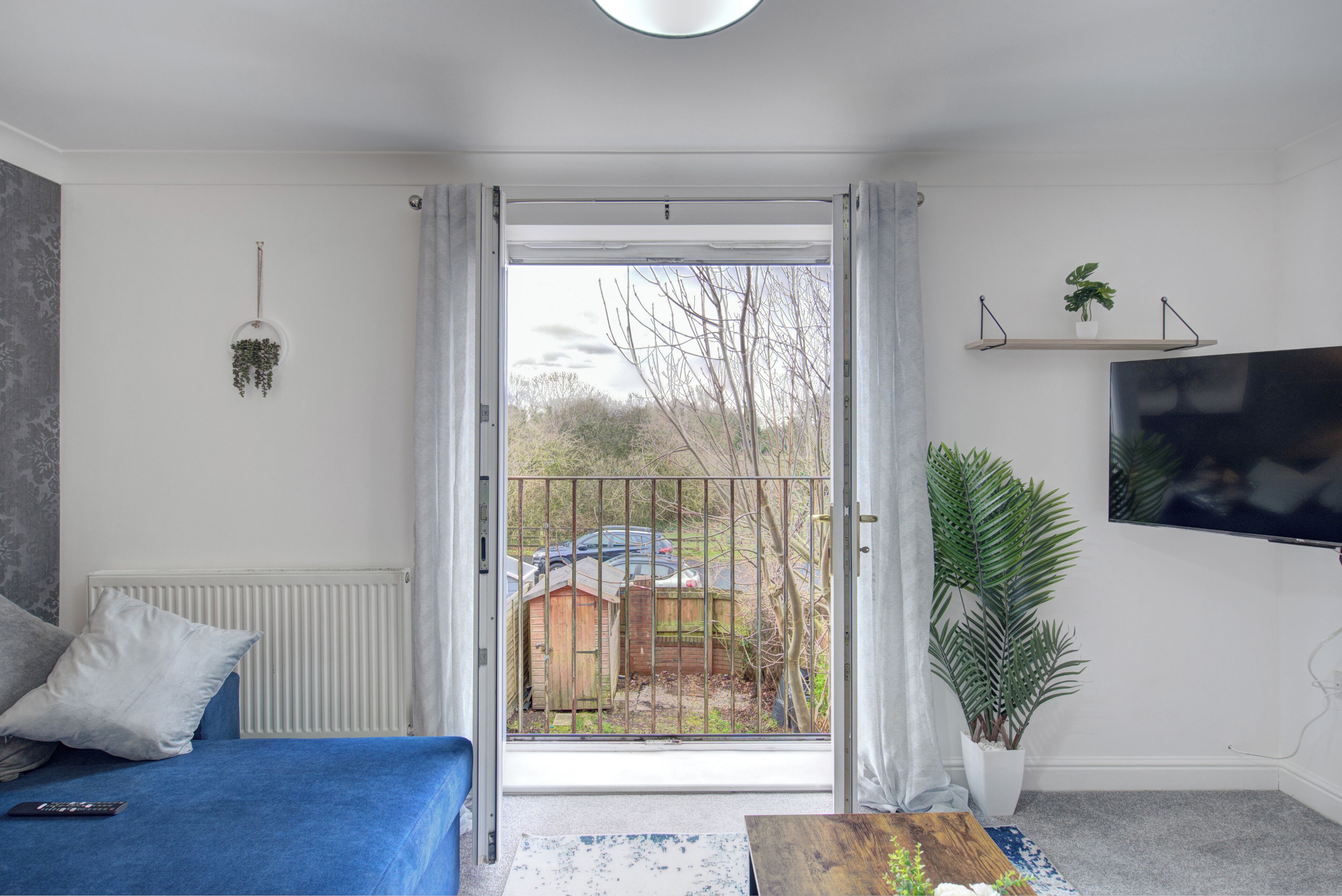 A modern living room with a blue sofa, a coffee table, and a view through a glass door to a garden.