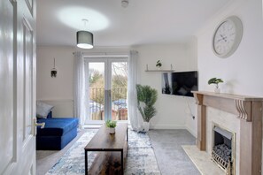 A living room with a blue sofa, a wooden coffee table, a fireplace, and a television mounted on the wall.