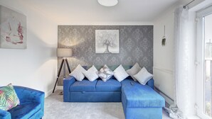 Un salón moderno con un sofá azul, una lámpara de pie y un ventanal grande.