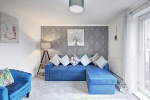 Ein modernes Wohnzimmer mit blauem Sofagarnitur, einer Stehlampe und einem großen Fenster.