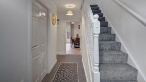 Un pasillo con una escalera alfombrada y un comedor al fondo.