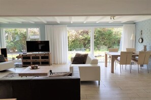 A living room with a TV, sofa, coffee table, and dining area with chairs and a table. - Family Villa with Jacuzzi & Large Garden (Balkbrug)